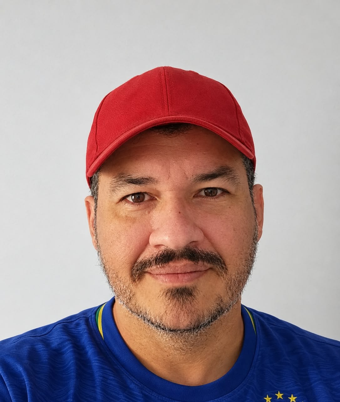 Homem usando boné vermelho e camisa azul da seleção, com barba curta e expressão neutra.